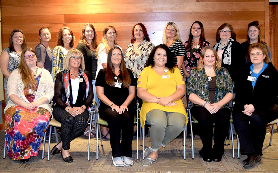 Mosaic Life Care School at Work, 2018 Graduates (16 women shown in two rows with the back row standing. There are 10 in the back row and 6 seated in the front row. The group is smiling and are posed toward the camera